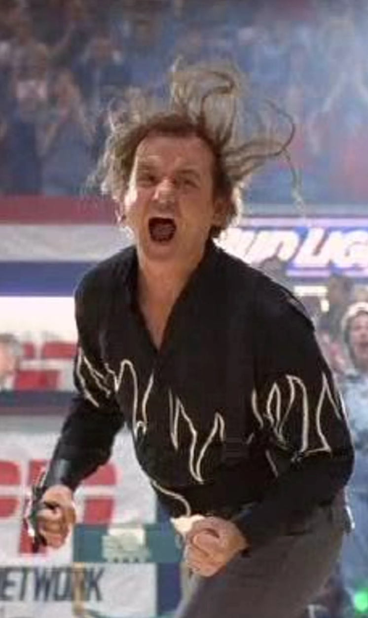 A man with disheveled hair and an intense expression is shown in a stadium, appearing to be shouting or shouting with his mouth wide open.