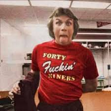 A person wearing a red t-shirt with the text "Fifty Fucking Yankees" is shown in a room with a sink and a flag visible in the background.