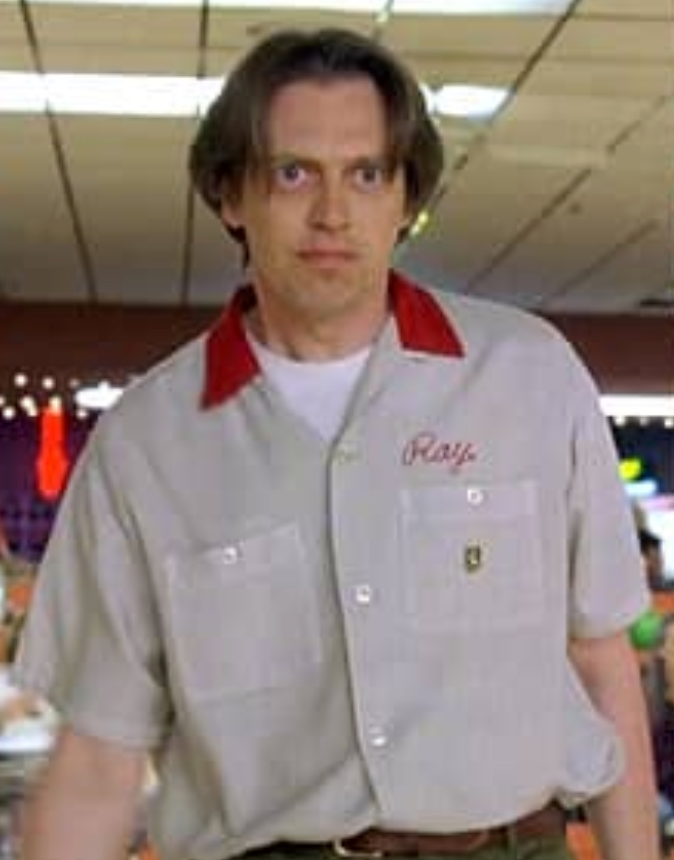 A man wearing a gray shirt with a red collar and the name "Ray" printed on it, standing in a bowling alley.