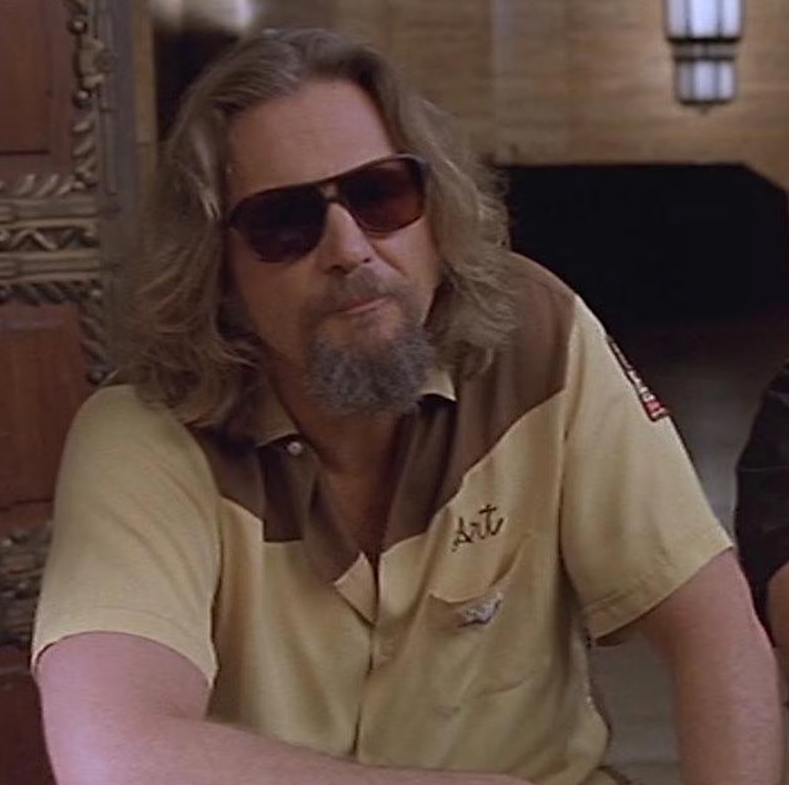 A man with long hair and sunglasses is sitting in a room, looking directly at the camera.