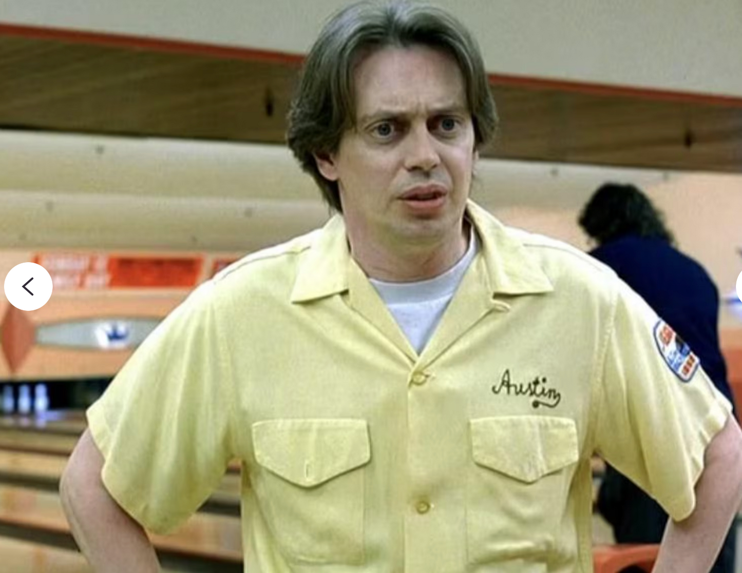 A man wearing a yellow shirt with the name "Austin" on it, standing in a bowling alley.