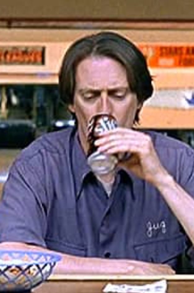 A man in a blue shirt is sitting at a table, drinking from a glass.