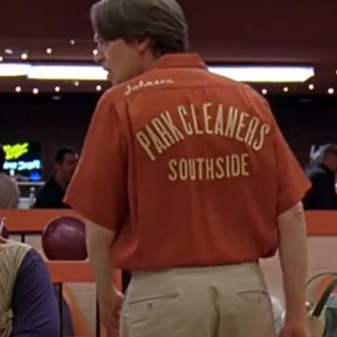 a man wearing a red shirt with the text "Park Cleaners Southside" printed on it, standing in what appears to be a bowling alley or similar venue.